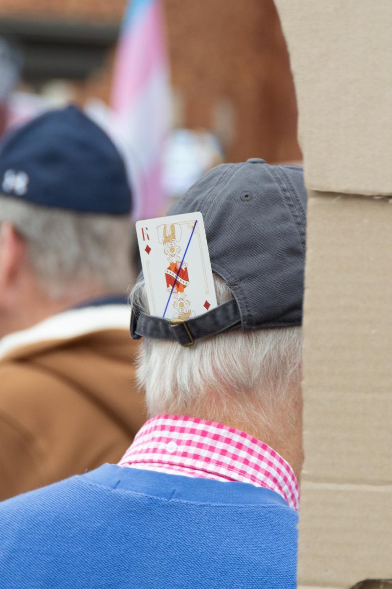 A crossed out king from a deck of cards sits tucked in an elderly protester's hat.