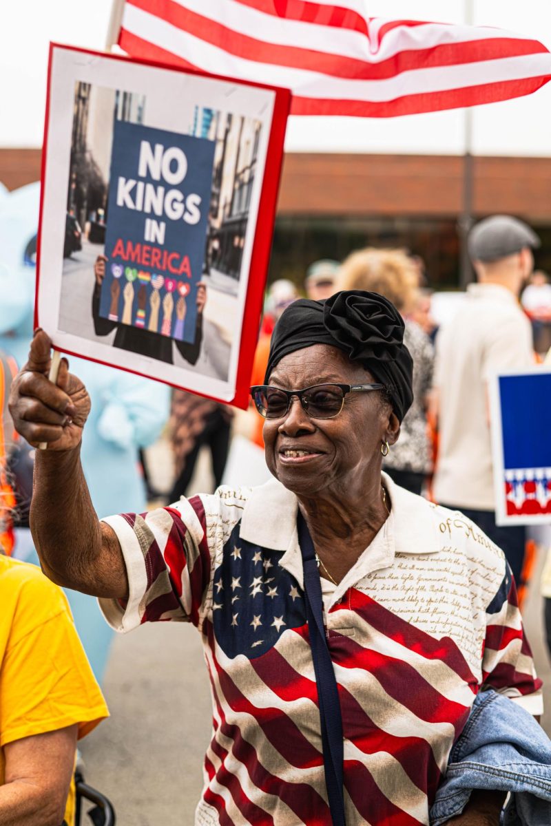 A protester waves their flag while holding a “No Kings in America” sign