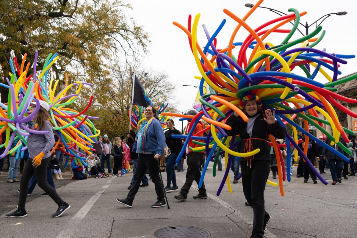 People adorned in dozens of long balloons march and wave in the 15th annual C-U Pride Parade in downtown Urbana on Saturday.