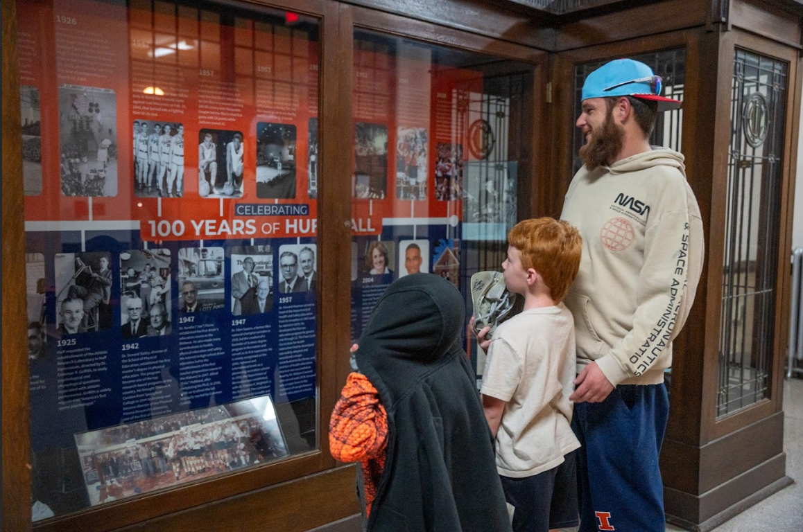 Kyle Kostro, Walgreens store manager and lifelong CU resident reads the Huff Hall centennial display case with his two sons on Oct. 23.