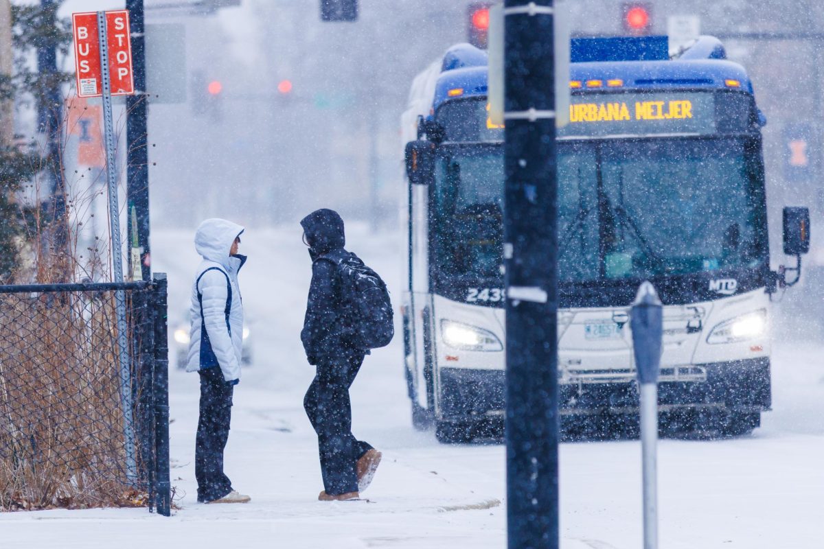 Two people stand in front of bus in snowy conditions on Jan. 24. The University encouraged remote classes Monday, but did not cancel all in-person meetings.