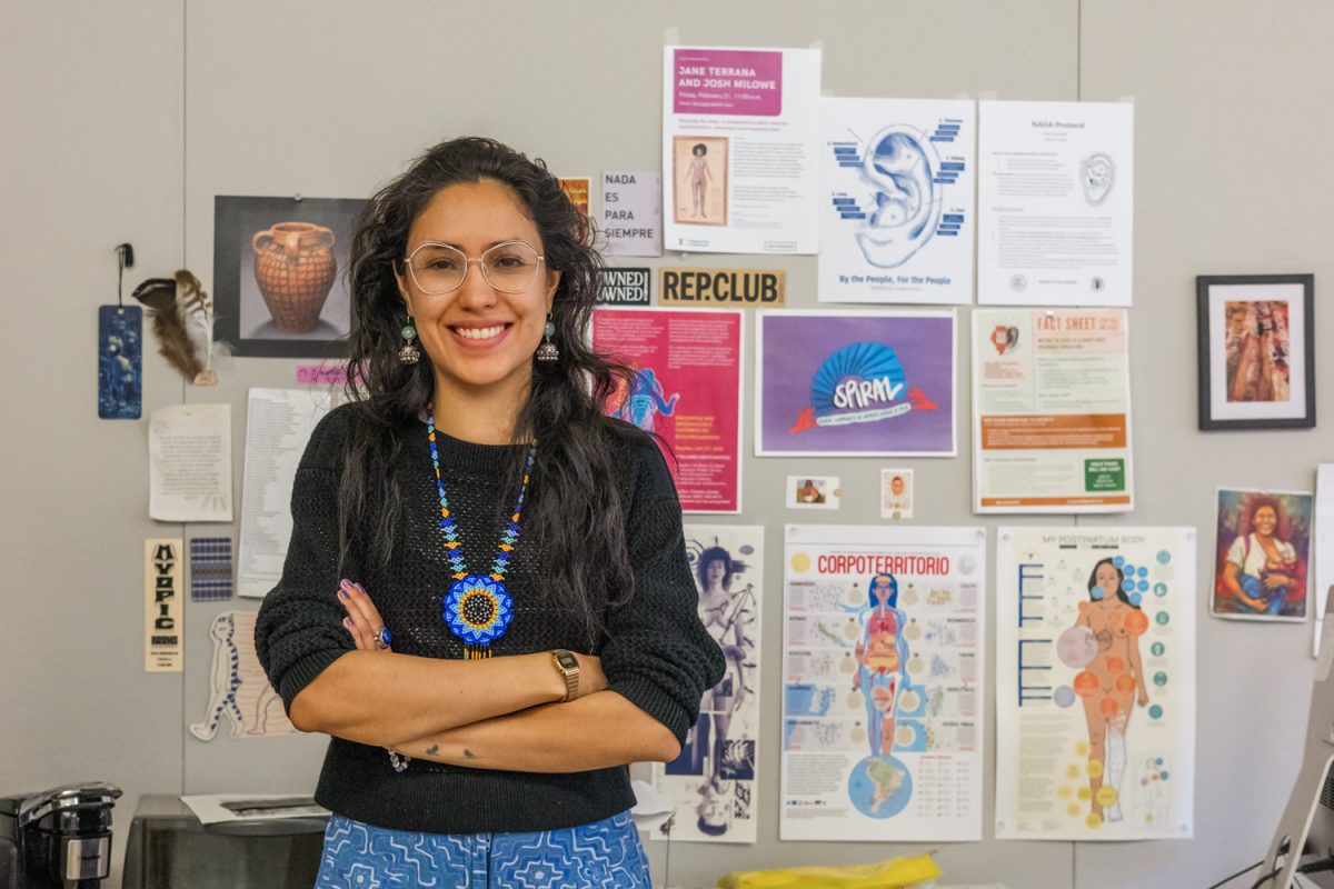 Catalina Alzate poses in front of several posters and decorations covering her office wall on Nov. 14, 2025. She uses art to create body maps, which are visual representations of internal experiences and sensations. 