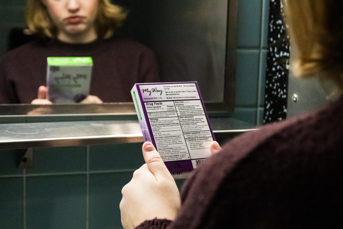 A young woman reads the label on a box of emerency contraception pills in a bathroom. The medication is available at vending machines in the Illini Union and at McKinley Health Center.