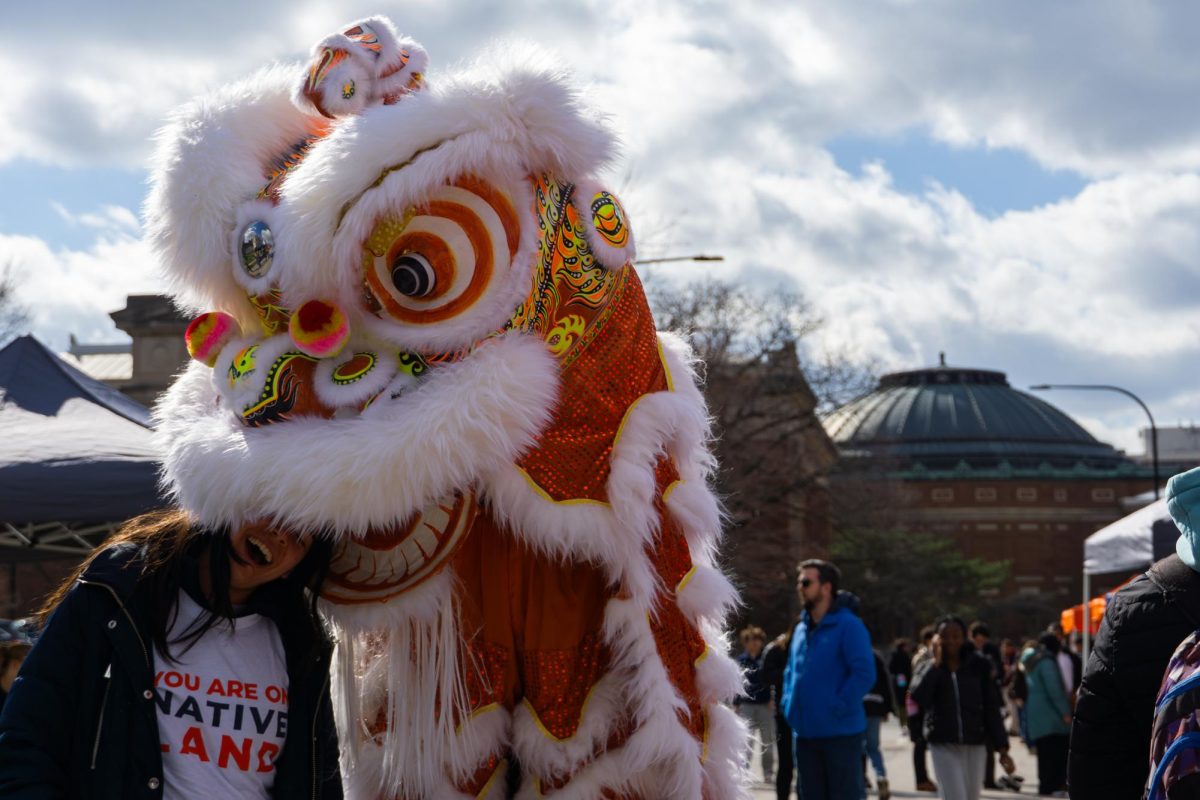 Two people in a dragon costume pretend to bite the head of an attendee of the first Crossroads of Culture event on March 27 on Nevada Street. Many cultural houses took part in the event hosted by Illinois Student Council, including the Asian American Cultural Center.