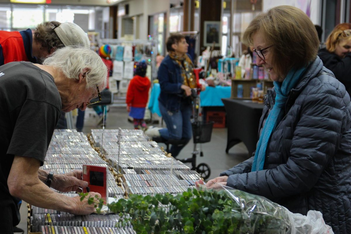 Booth owner Dan Hughes, (right) helps customer look for CDs at his booth during the Middlefork Flea Market held in Lincoln Square Mall in Urbana on Saturday, Oct. 25, 2025. Hughes, a retired broadcasting teacher at Parkland College, sells a wide variety of CD at the festival ranging several genres.