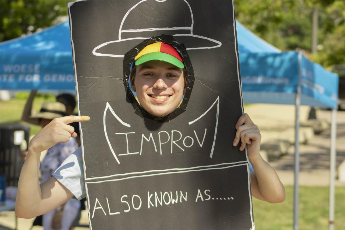 David Hopping, a PhD student in informatics and the founder of the improv group Also Known As poses with a sign on Quad Day on Aug. 8. 2024.