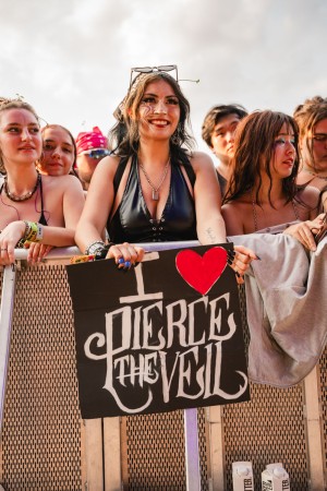 A fan at the front against the barricade holds a sign displaying appreciation for the band.