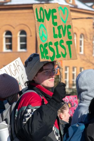 A student holding a sign made of a stick and cardboard, reading "Love Live Resist." Many people gathered with signs similar to this in front of Alma Mater at 2 p.m. on Jan. 30.