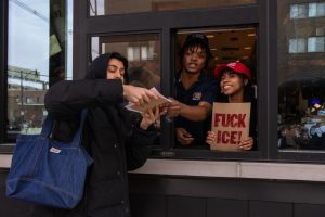 Raising Cane's employees hold up a sign reading "FUCK ICE!" and give out free drink coupons to anti-ICE protesters as they march down Green Street on Jan. 30.