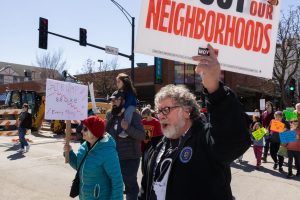A protester holds up a sign reading “Protect Our Neighborhoods” while chanting with a crowd gathered at the 3rd No Kings protest outside of the Champaign County Courthouse on Saturday.