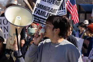 A protester speaks into a megaphone as others hold signs advocating for immigrant rights during the No Kings 3 protest in downtown Urbana Saturday afternoon.