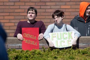A couple of protesters hold signs reading “Chinga La Migra” and “Fuck I.C.E” during the No Kings 3 protest in downtown Urbana Saturday afternoon.